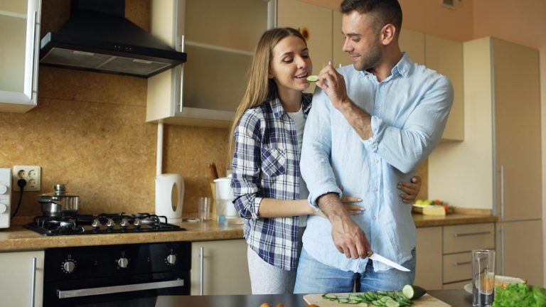 Happy young couple embracing and talking in the kitchen while cooking breakfast at home in the morning