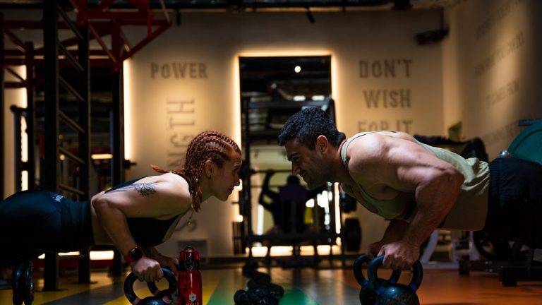 a man and a woman doing push ups with kettles
